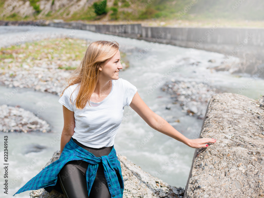 Young woman sitting on rock in fast mountain river and splashing on summer or early autumn outdoor copy space background