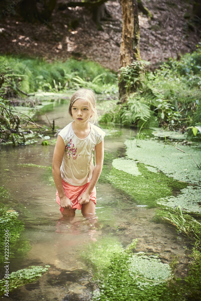 Fototapeta premium Child cute blond girl playing in the creek. Girl walking in forest stream and exploring nature. Summer children fun. Children summer adventure