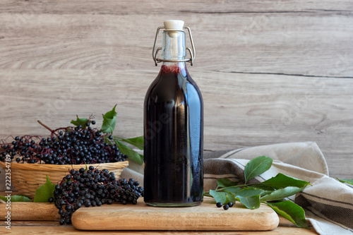 A bottle of black elder syrup with fresh elderberries