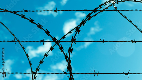 Barbed wire against blue sky and clouds.