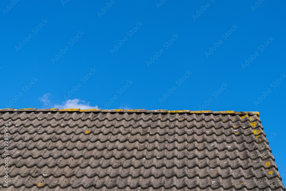 Roof with grey roof tiles and a clear blue sky with some clouds on a sunny day Roof with grey roof tiles and a clear blue sky with some clouds on a sunny day