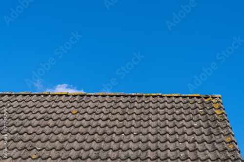 Roof with grey roof tiles and a clear blue sky with some clouds on a sunny day