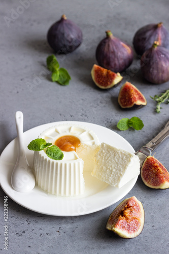 Ricotta cheese on white plate with figs, honey, mint and thyme on grey concrete background. Copy space for text.