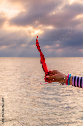 Girl holding a glass with wine uring the sunset on the sea photo