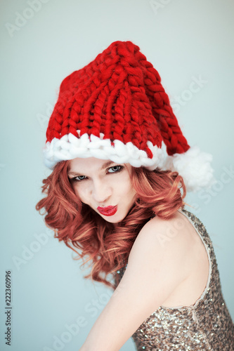 Santas little helper. Beautiful happy young woman with a santa claus hat, perfect make up, red lipstick, can be used as background