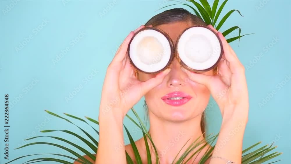 Beauty girl with coconuts. Exotic young woman portrait. Coconut fruit oil and green palm tree leaf on blue background. Healthy food, skin care concept. Slow motion 4K UHD video 3840x2160 Beauty girl with coconuts. Exotic young woman portrait. Coconut fruit oil and green palm tree leaf on blue background. Healthy food, skin care concept. Slow motion 4K UHD video 3840x2160