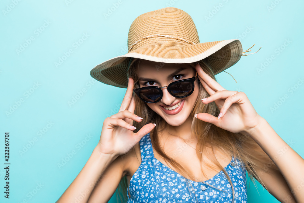 Close-up of pretty joyful girl in straw hat ready for journey posing over blue background.