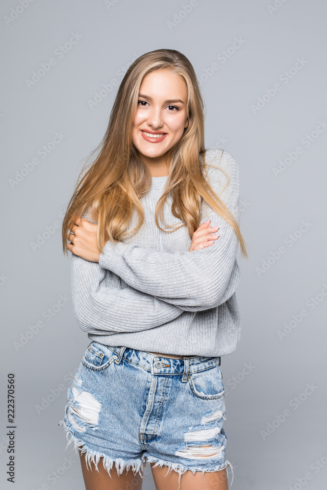 Portrait of a cheerful young woman in sweater smiling with arms crossed on gray background Portrait of a cheerful young woman in sweater smiling with arms crossed on gray background