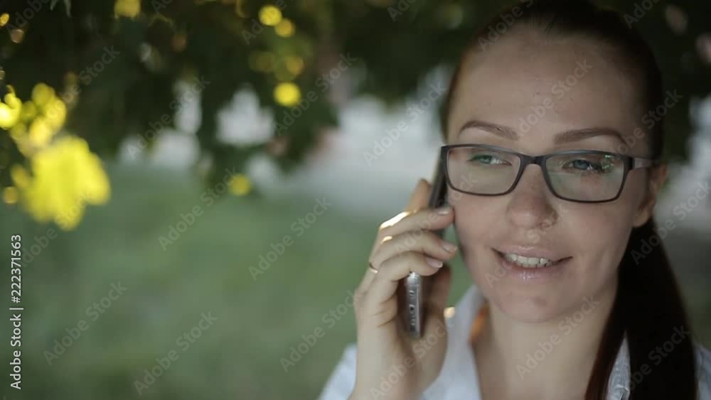 a business Caucasian middle-aged woman with red hair in optical glasses and a white blouse makes an important phone call while on the street of the city. a business Caucasian middle-aged woman with red hair in optical glasses and a white blouse makes an important phone call while on the street of the city.