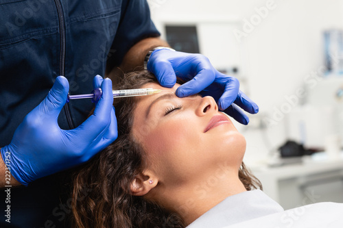 Close up of beautician expert's hands injecting botox in female forehead. photo