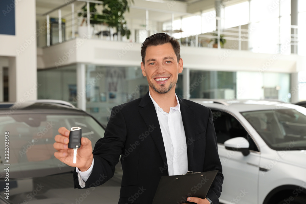 Salesman with clipboard and car key standing in salon Salesman with clipboard and car key standing in salon