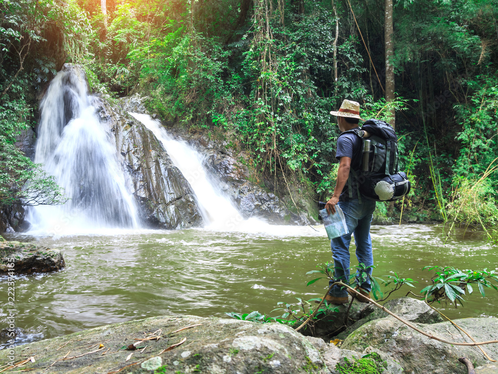 male hiker with backpack holding map looking nature waterfall in forest