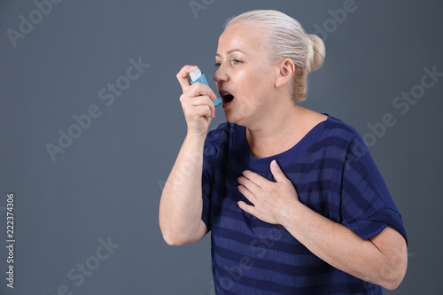 Woman using asthma inhaler on color background with space for text