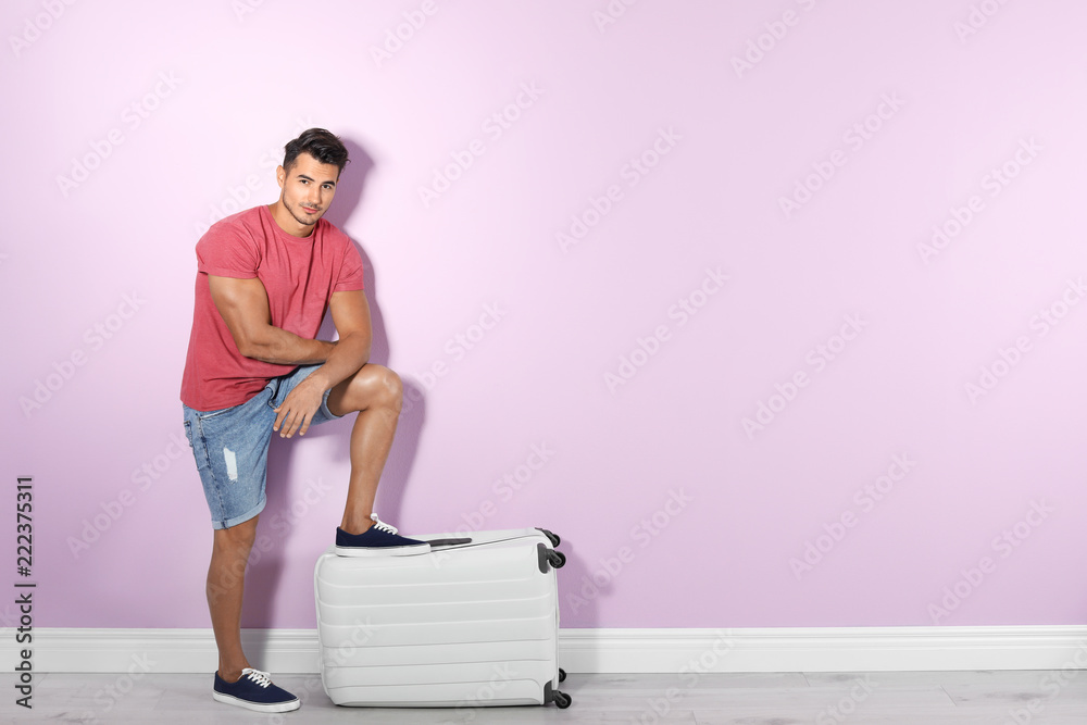 Young man with suitcase on color wall background. Space for text Young man with suitcase on color wall background. Space for text