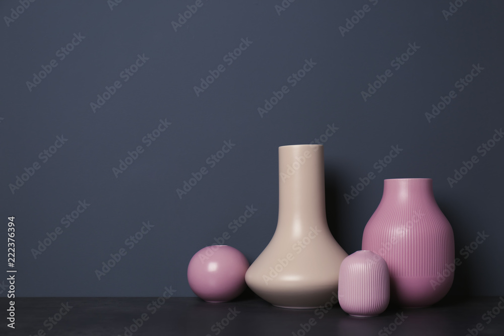 Beautiful ceramic vases on table against color wall with space for text