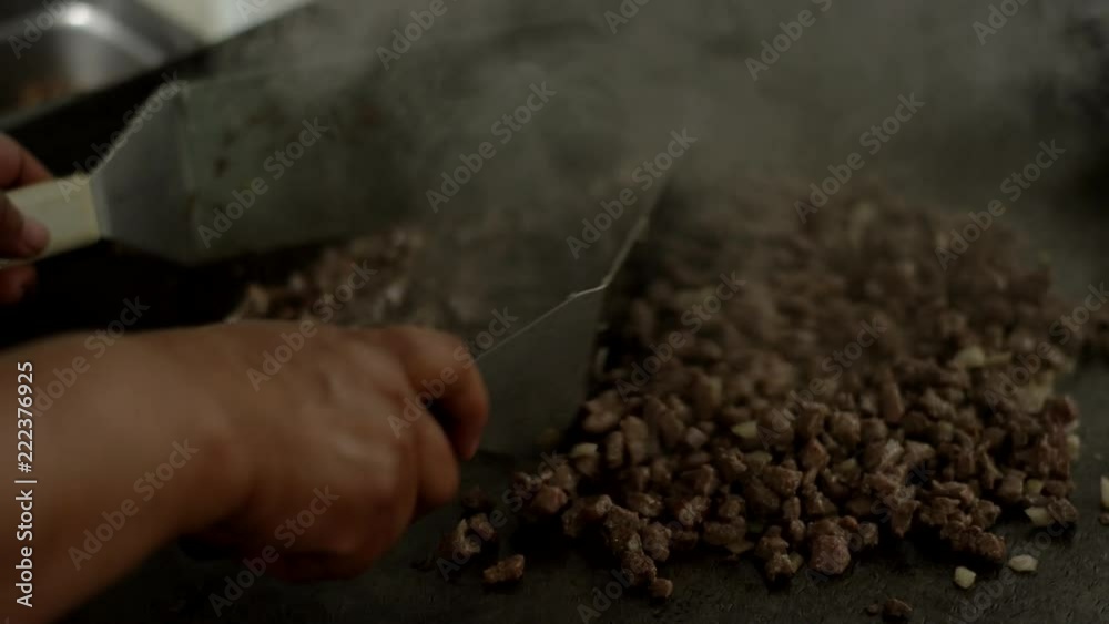 Close up of a woman chopping carne asada steaming on a flat grill In a Mexican food restaurant kitchen
