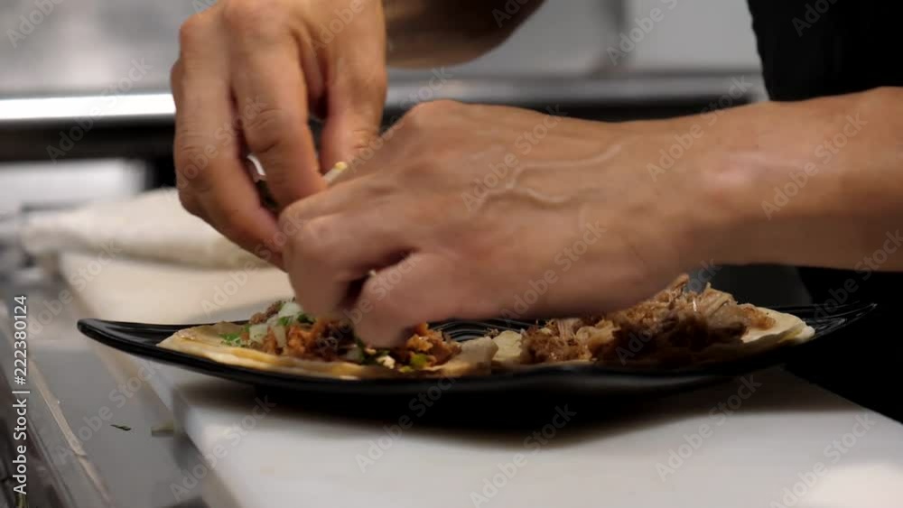 Close up shot of a Hispanic hands preparing an order of carnitas tacos in the kitchen of a Mexican restaurant and placing the plate on the counter