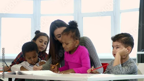 Cheerful young female teacher and her little students at school classroom