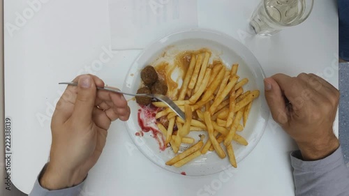 a bearded middle-aged Caucasian male is sitting in a fast food cafe in a shopping center, eating fried potatoes and meat meatballs. photo