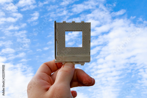 White Hand Holding Computer Part Against Blue Sky with Clouds