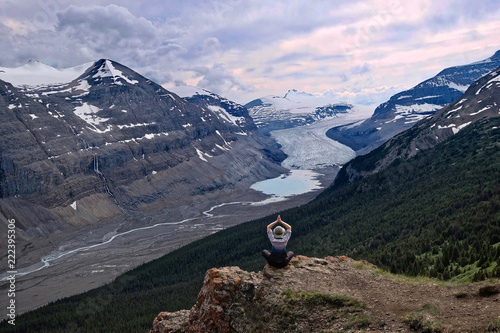Woman meditating on steep cliff over Columbia Icefield glacier and a moraine lake.  Outdoor yoga in  Banff  Jasper National Park. Canadian Rocky Mountains.  Patterson Ridge trail. Alberta. Canada. photo