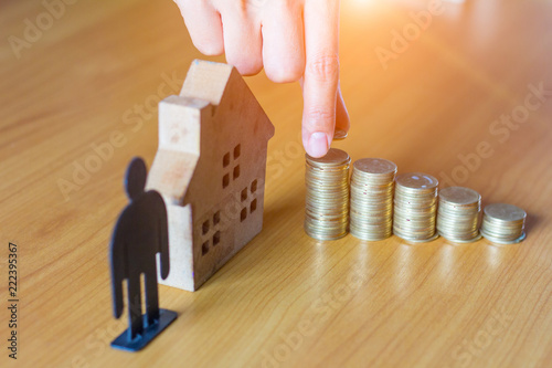Hand putting money coin stack with wooden house; Property investment and house mortgage financial concept,