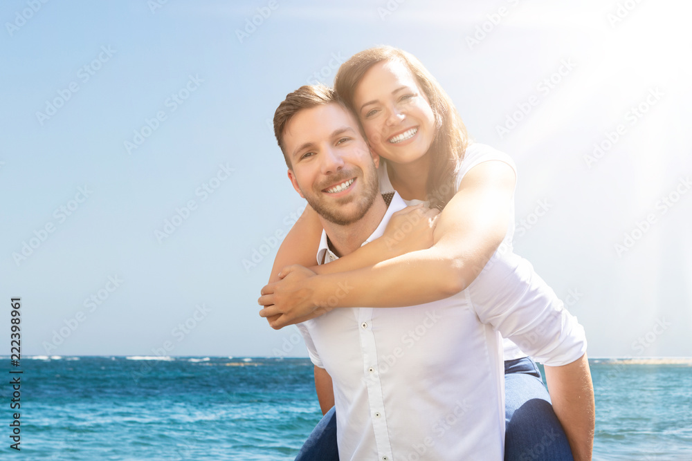 Happy Man Giving Piggyback To His Wife At Beach