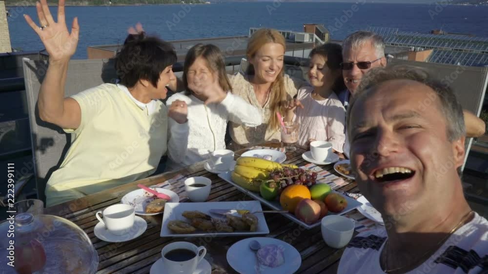 Big happy family takes a selfie or Uses Phone Video Call Camera sitting on the open terrace on the roof of the house on the sea coast. Big happy family takes a selfie or Uses Phone Video Call Camera sitting on the open terrace on the roof of the house on the sea coast.