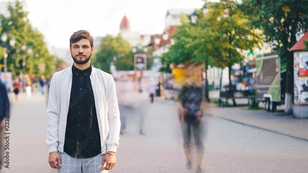 Time-lapse of handsome guy towny standing in the street downtown and looking at camera with people running around. Urban lifestyle, solitude and society concept. Time-lapse of handsome guy towny standing in the street downtown and looking at camera with people running around. Urban lifestyle, solitude and society concept.