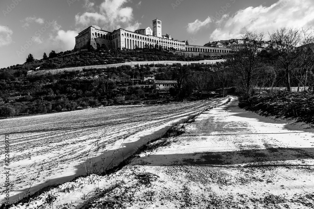 View of Assisi town (Umbria) in winter, with a field covered by snow and sky with white clouds