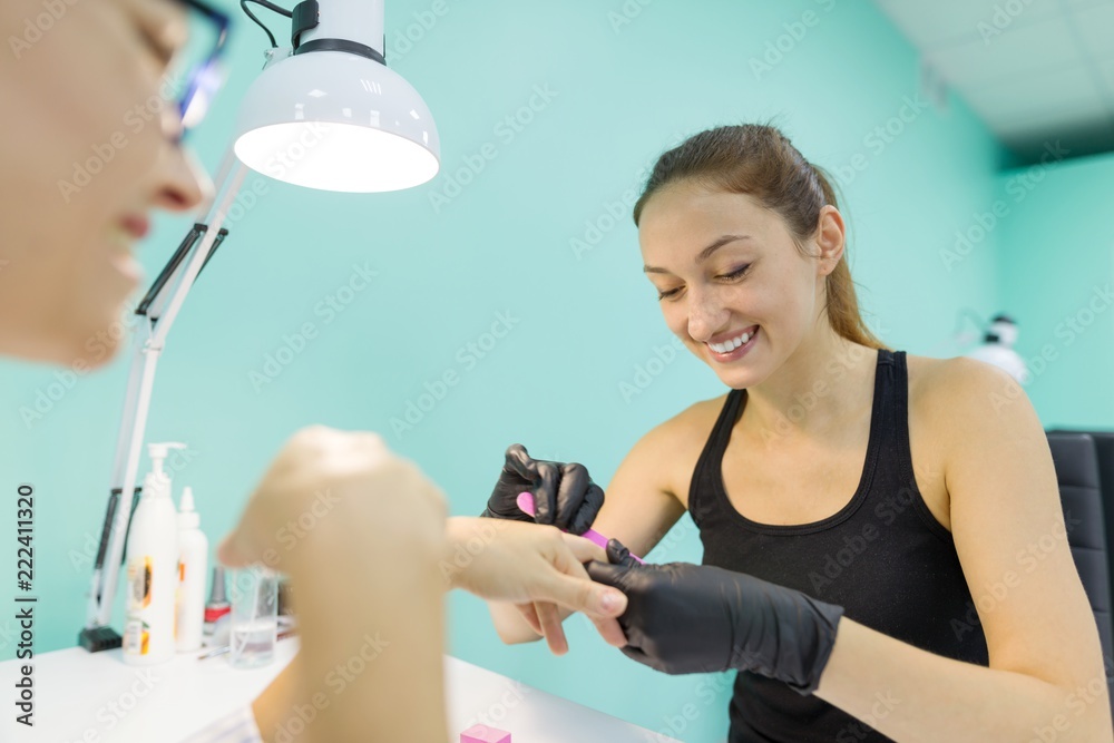 Woman in nail salon receiving manicure by manicurist, closeup manicure process. Nail and hand care in beauty salon. Woman in nail salon receiving manicure by manicurist, closeup manicure process. Nail and hand care in beauty salon.