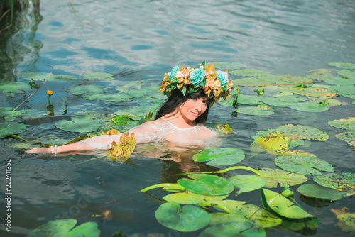 Beautiful dark haired girl in white dress posing in river with water lilies. Fairytale story about modern ophelia 