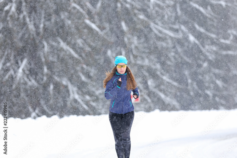 Young woman running on the mountain road in bad weather in winter. Beautiful girl jogging in blizzard or snowstorm Young woman running on the mountain road in bad weather in winter. Beautiful girl jogging in blizzard or snowstorm