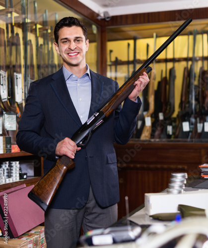 Handsome adult male in hunting shop with rifle in hands