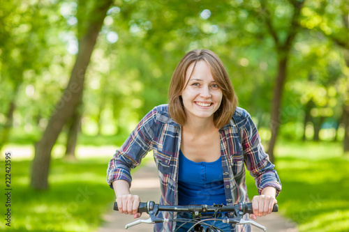 Happy young beautiful woman riding a bicycle in a park. Space for text