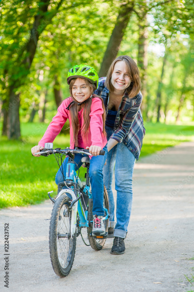 Obraz premium mom teaches her daughter to ride a bicycle in the park