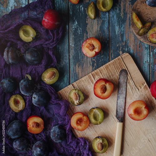 Fresh organic plums and plum slices on wooden board and rustic wooden table, autumn harvest, seasonal fruits, healthy lifestyle, top view, selective focus