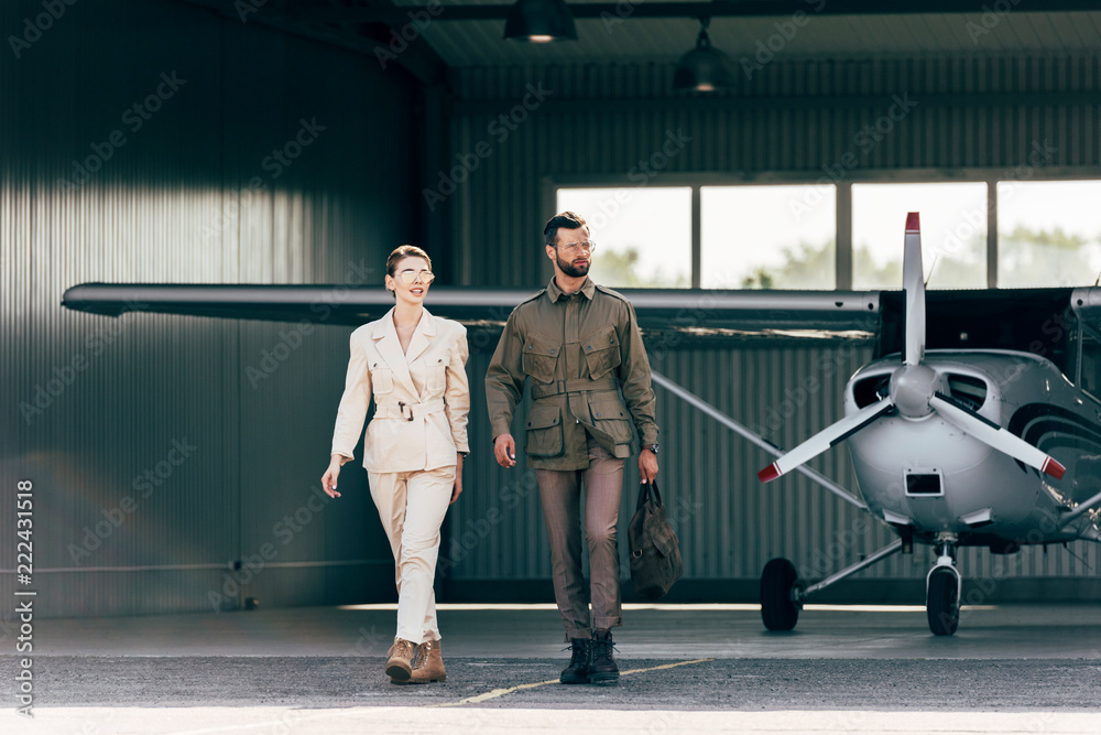 handsome man carrying bag and walking with stylish girlfriend near hangar with plane handsome man carrying bag and walking with stylish girlfriend near hangar with plane