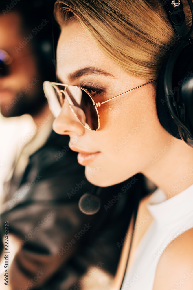 selective focus of beautiful woman in sunglasses and headset sitting near male pilot in cabin of airplane selective focus of beautiful woman in sunglasses and headset sitting near male pilot in cabin of airplane