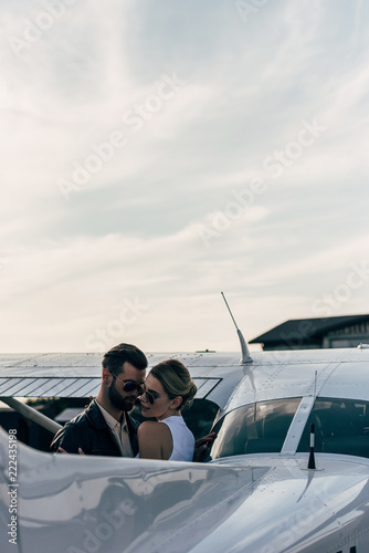 serious handsome man in leather jacket and sunglasses embracing attractive girlfriend near airplane © LIGHTFIELD STUDIOS