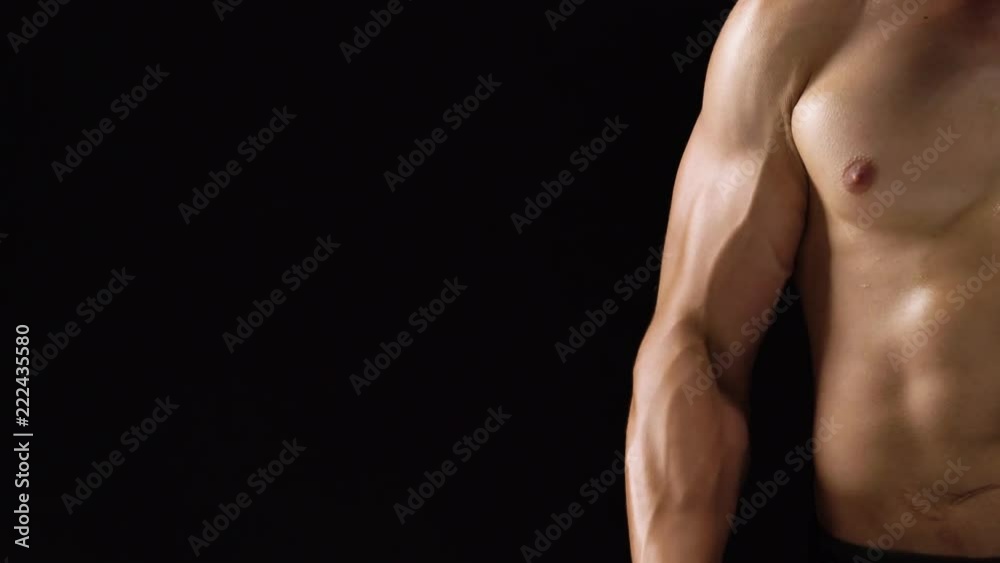 Man flexes his hands with dumbbells, training his biceps on a black background in the studio. Half body in the frame Man flexes his hands with dumbbells, training his biceps on a black background in the studio. Half body in the frame
