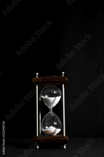 Hourglass, or sand clock isolated in black background, in low light condition.