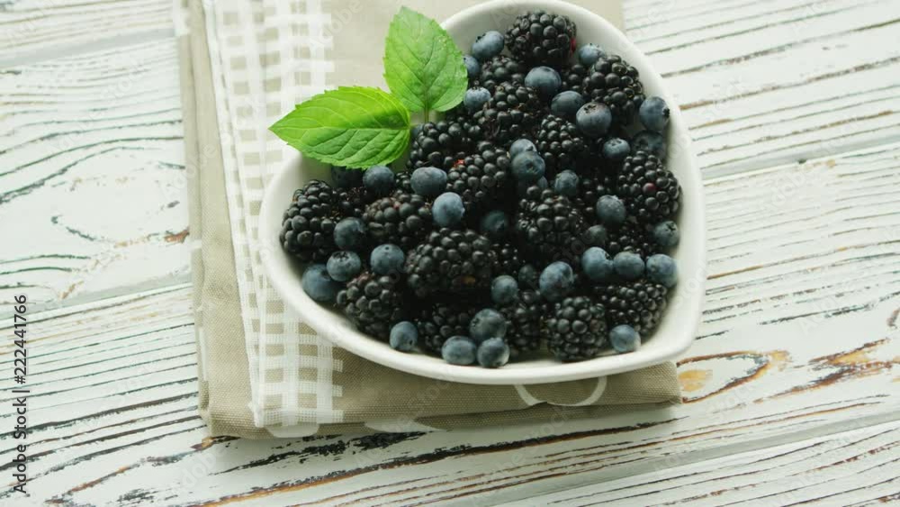 From above blueberry and blackberry with green leaf in heart shaped bowl on wooden background From above blueberry and blackberry with green leaf in heart shaped bowl on wooden background