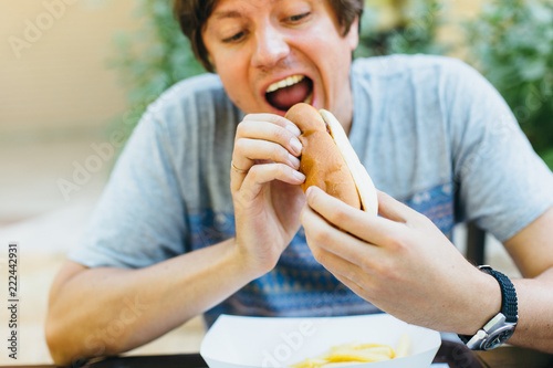 Portrait of young handsome man eating hotdog in cafe .