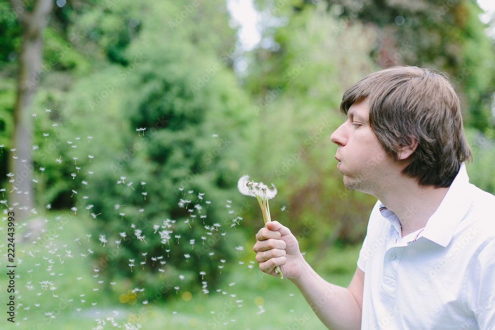 Young handsome man blowing dandelion flower in summer forest Young handsome man blowing dandelion flower in summer forest