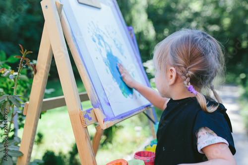 Little cute girl painting on the easel outdoors in the garden photo