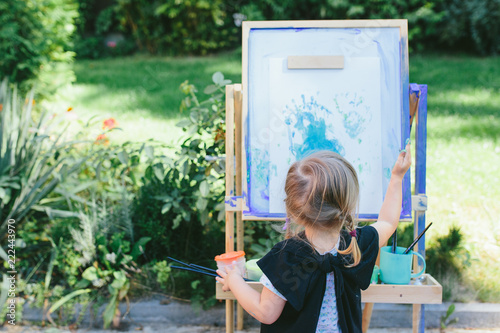 Little cute girl painting on the easel outdoors in the garden photo