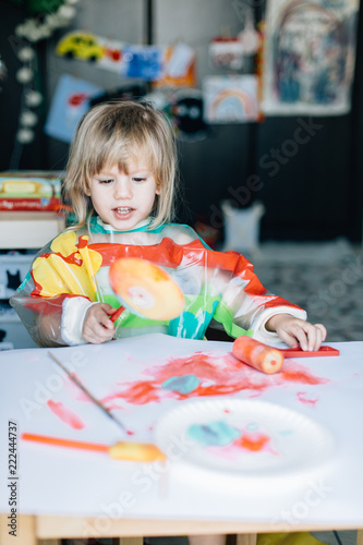 Portrait of adorable baby girl drawing with paints sitting at the table.