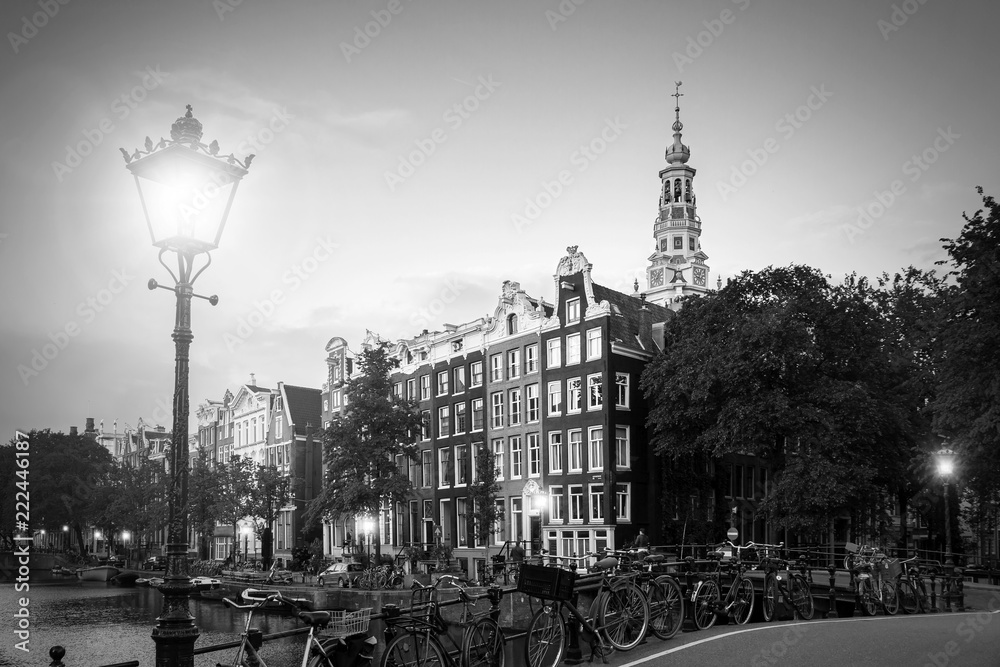 Beautiful view of a lantern on a bridge and the Southern Church in the background at the famous UNESCO world heritage canals of Amsterdam, the Netherlands, in black and white.
