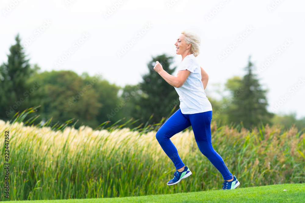 Fit athletic mature woman running alongside reeds Fit athletic mature woman running alongside reeds